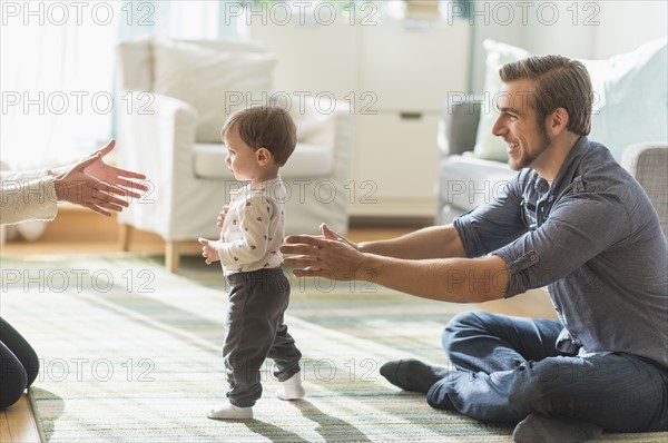 Happy parents helping little son (2-3 years) walking in living room.