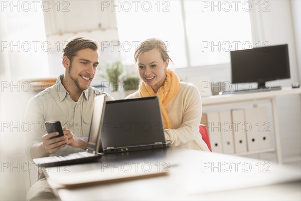 Young man and woman working together with laptop in office.