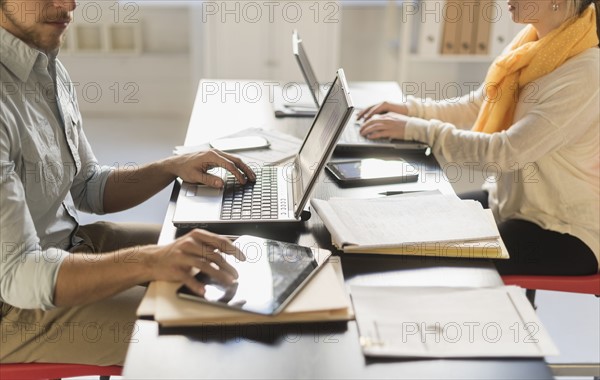 Close up of young man and woman working with laptops at desk.