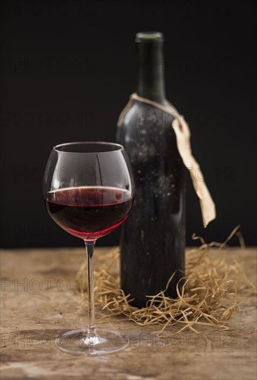 Still life with red wine glass and bottle on wooden table, studio shot.