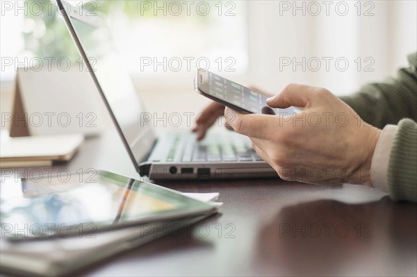 Close up of man's hands working at desk with electronic devices.