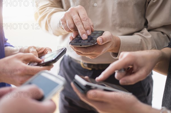 Close up of hands of men and women using smartphones together.