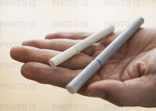 Close up of man's hand holding cigarette and e-cigarette.