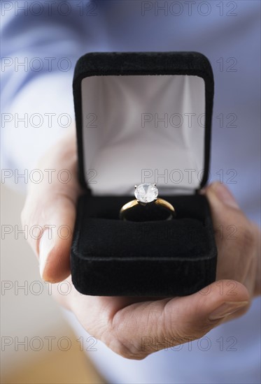 Close up of man's hand holding open box with engagement ring.