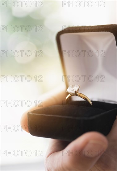 Close up of man's hand holding open box with engagement ring.