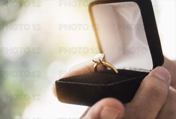 Close up of man's hand holding open box with engagement ring.