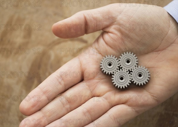 Close up of man's hand holding metal cogs.