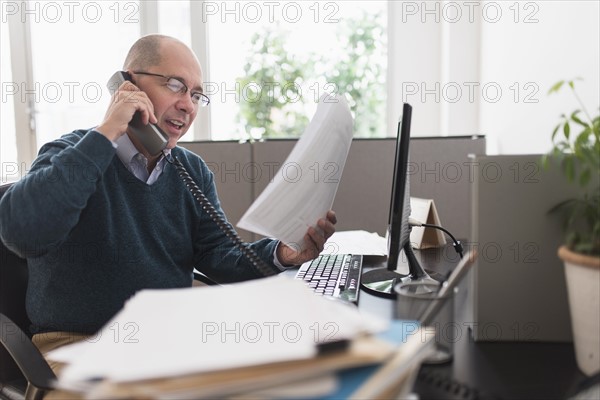 Mature businessman using landline phone in office.