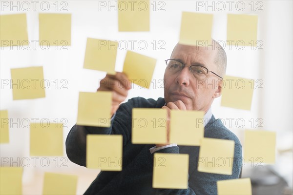 Businessman arranging adhesive notes on glass wall.