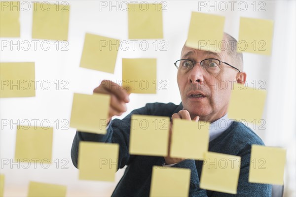 Surprised businessman arranging adhesive notes on glass wall.