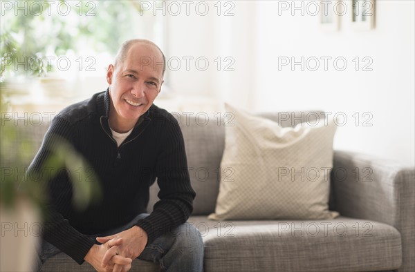 Portrait of smiling mature man relaxing on sofa in living room .