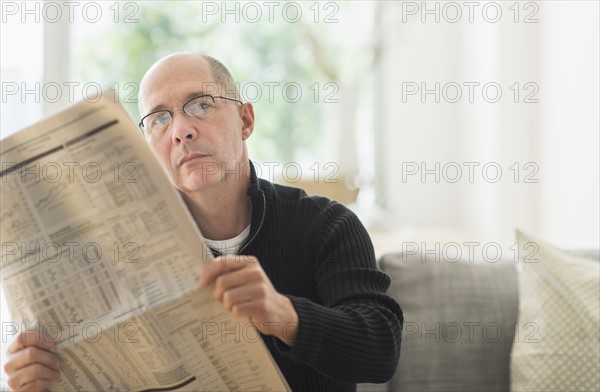 Mature man reading newspaper on sofa .
