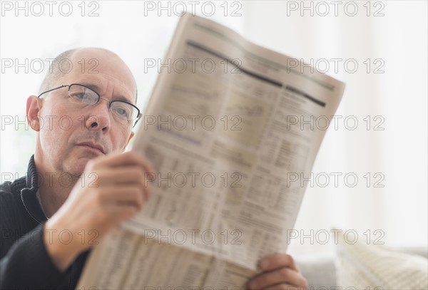 Mature man reading newspaper on sofa .