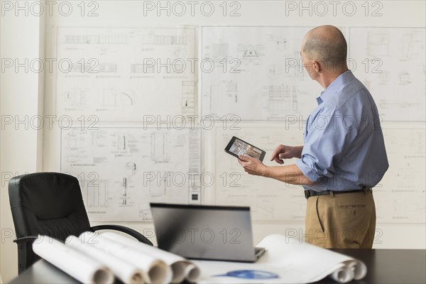 Mature architect looking at blueprints in office.