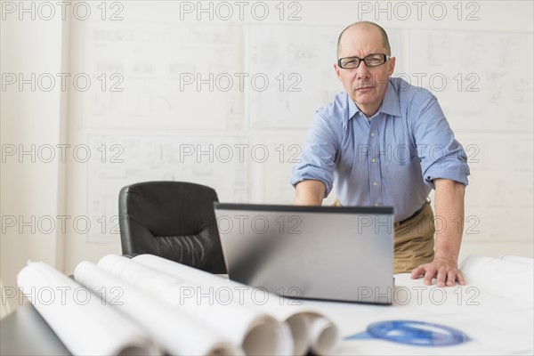 Portrait of mature architect using laptop in office.