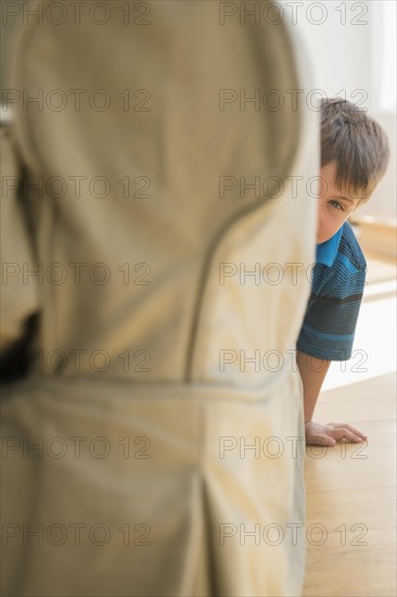 Boy (6-7) peeking around side of sofa