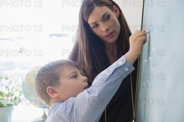Female teacher assisting schoolboy (6-7) while writing on blackboard