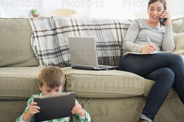 Mother and son (6-7) sitting in living room with tablet and laptop