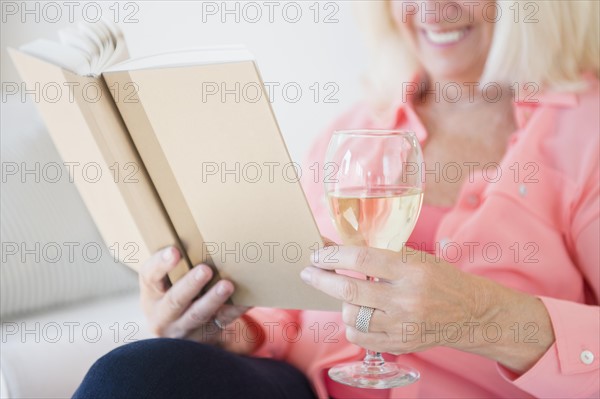 Senior woman reading book and drinking wine