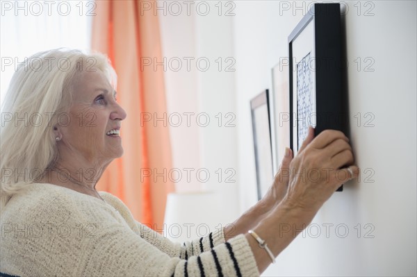 Senior woman hanging picture frame on wall