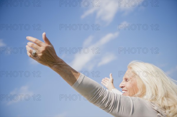 Senior woman with arms outstretched against sky