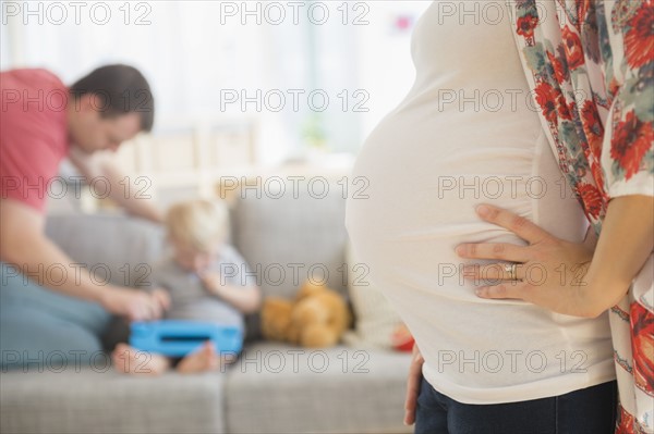 View of pregnant woman in living room, father and son (2-3) in background