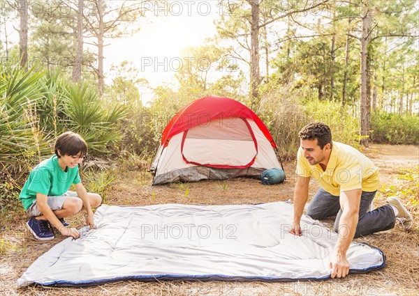 Father and son (12-13) preparing sleeping bag for camping