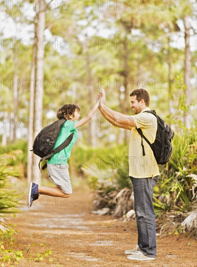 Father and son (12-13) doing high five in forest