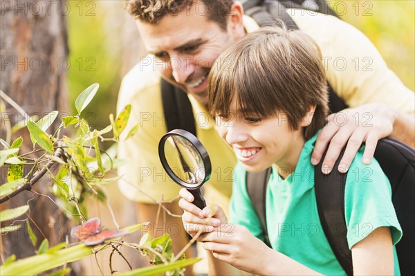 Father and son (12-13) watching butterfly with magnifying glass