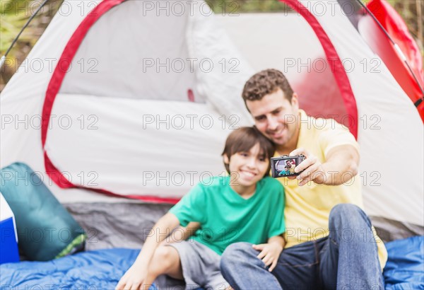 Father and son (12-13) taking selfie in front of tent