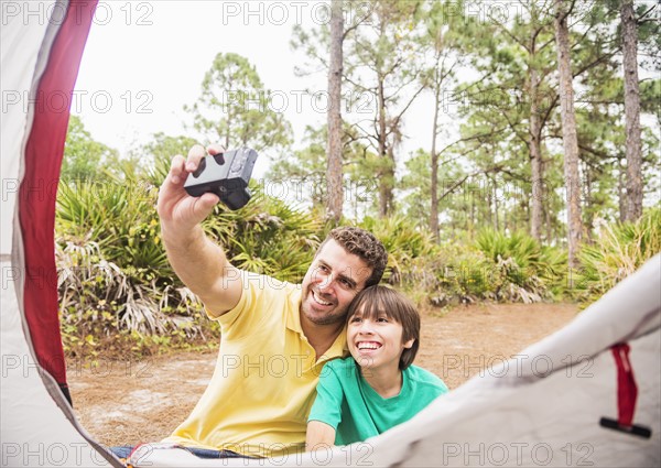 Father and son (12-13) taking selfie in front of tent