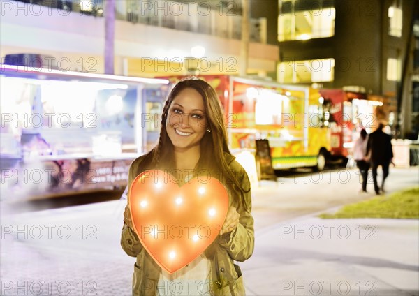 Woman in front of building and food truck holding illuminated heart
