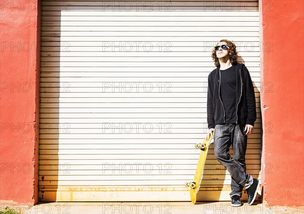 Man with skateboard leaning on garage door