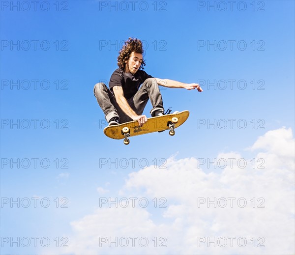 Man jumping on skateboard against sky and clouds