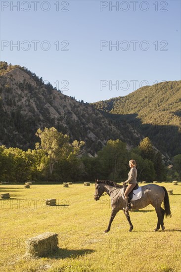 Woman horseback riding in field at sunset