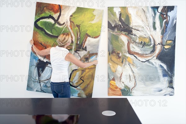 Woman hanging paintings indoors