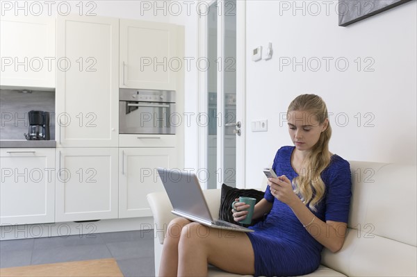 Young woman using cell phone and laptop at home