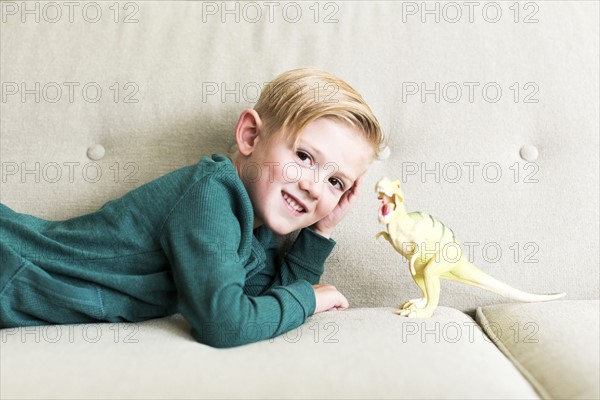 Boy (2-3) lying on sofa with toy dinosaur