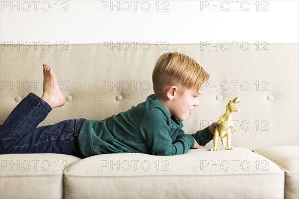 Boy (2-3) playing with toy dinosaur on sofa