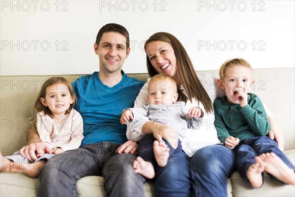 Portrait of family with three children (2-3, 4-5) sitting on sofa