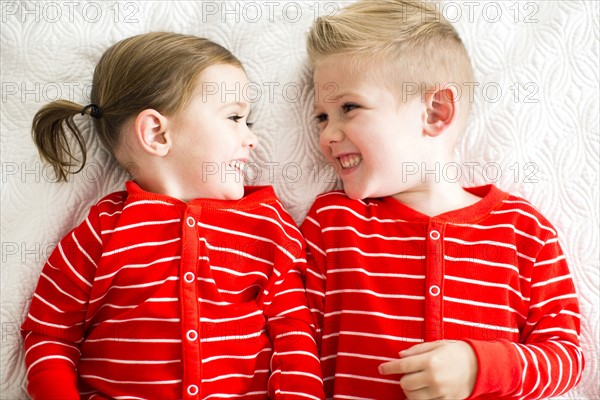 Siblings (2-3, 4-5) in red pajamas lying on bed