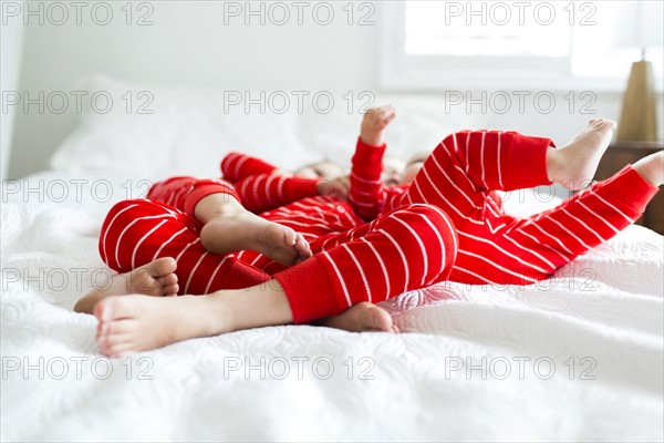 Siblings (2-3, 4-5) in red pajamas lying on bed