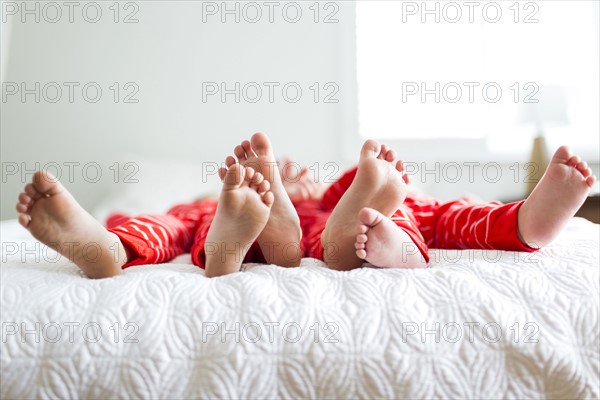 Siblings (2-3, 4-5) in red pajamas lying on bed