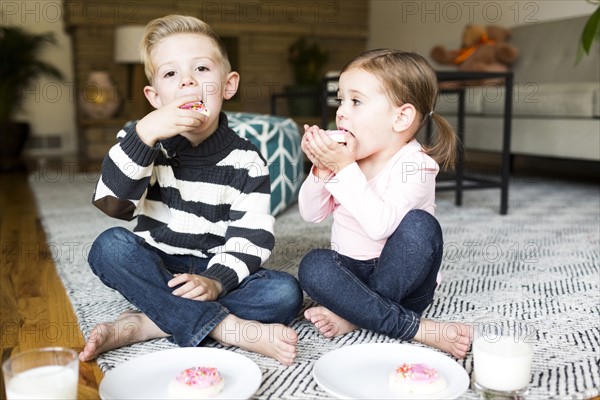 Brother (6-7) and sister (4-5) eating cookies in living room