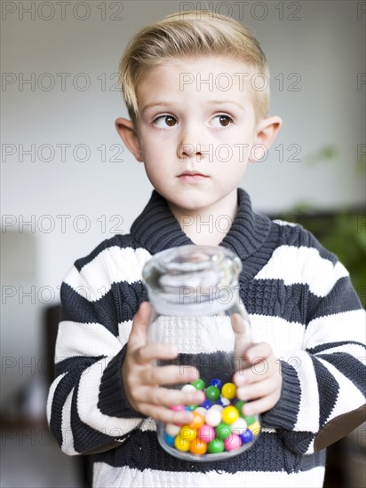 Boy (6-7) holding glass jar with candies