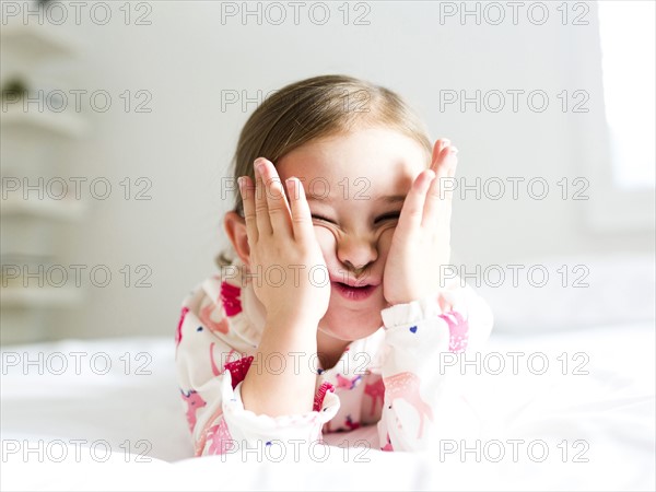 Girl (2-3) lying on bed pulling funny face