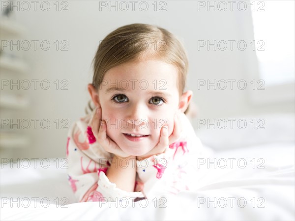 Girl (2-3) lying on bed holding head in hands