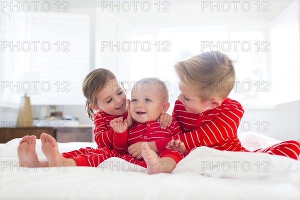 Boy (6-7) and girl (4-5) embracing brother (2-3) on bed
