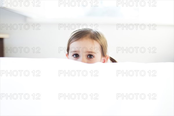 Girl (4-5) peeking over bed edge