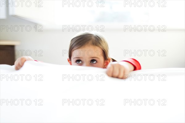 Girl (4-5) peeking over bed edge